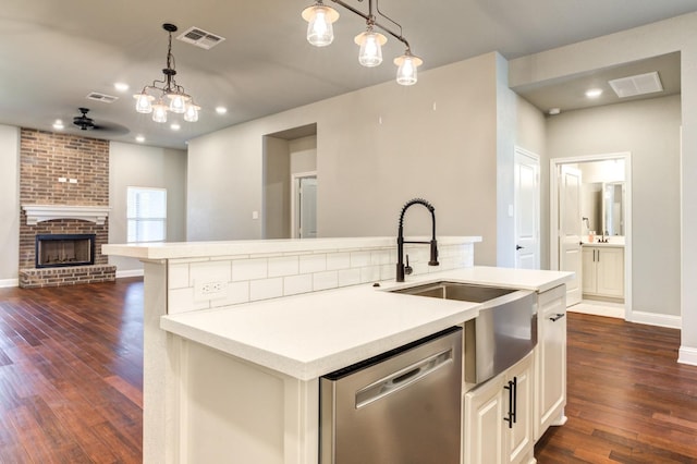 kitchen with dark wood-type flooring, sink, hanging light fixtures, a center island with sink, and dishwasher