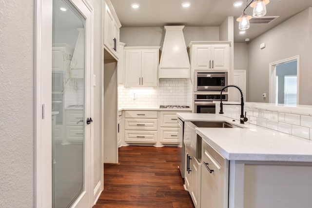 kitchen with premium range hood, white cabinets, decorative backsplash, stainless steel appliances, and dark wood-type flooring