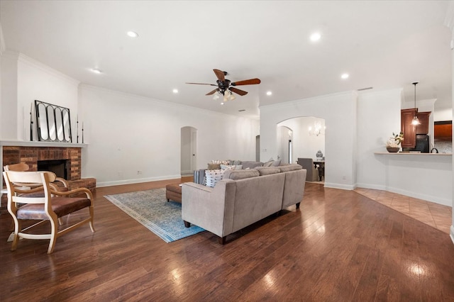 living room with dark hardwood / wood-style flooring, a brick fireplace, crown molding, and ceiling fan