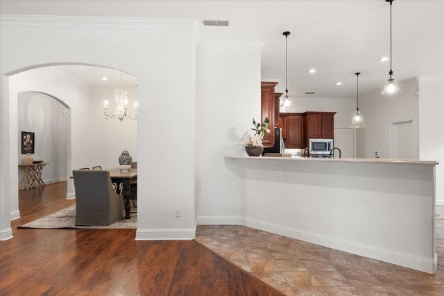 kitchen featuring dark wood-type flooring, stainless steel microwave, decorative light fixtures, and crown molding