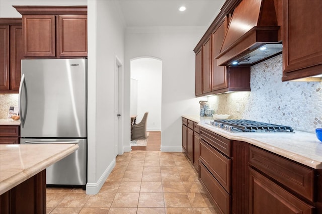 kitchen with light tile patterned floors, crown molding, premium range hood, stainless steel appliances, and decorative backsplash