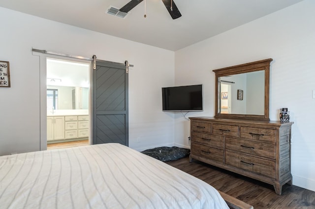 bedroom with dark wood-type flooring, ensuite bath, a barn door, and ceiling fan