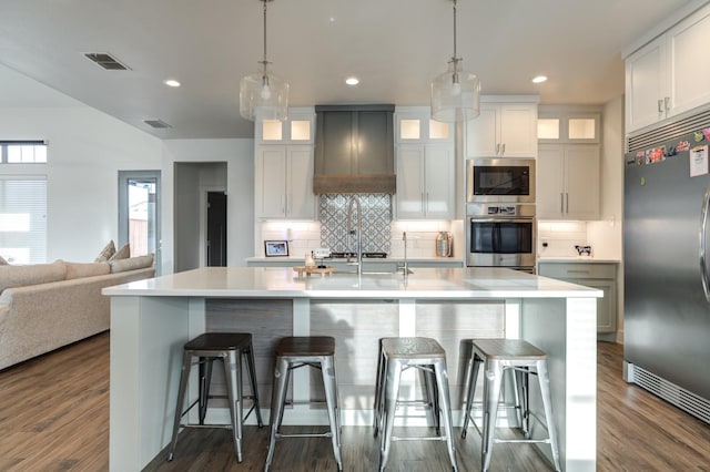 kitchen featuring stainless steel appliances, an island with sink, white cabinets, and a breakfast bar