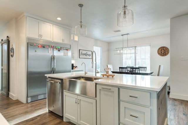 kitchen with pendant lighting, sink, stainless steel appliances, white cabinets, and a center island with sink