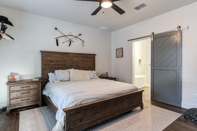 bedroom featuring ceiling fan, a barn door, dark hardwood / wood-style floors, and ensuite bath