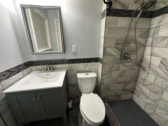 bathroom with vanity, toilet, tile walls, and a tile shower