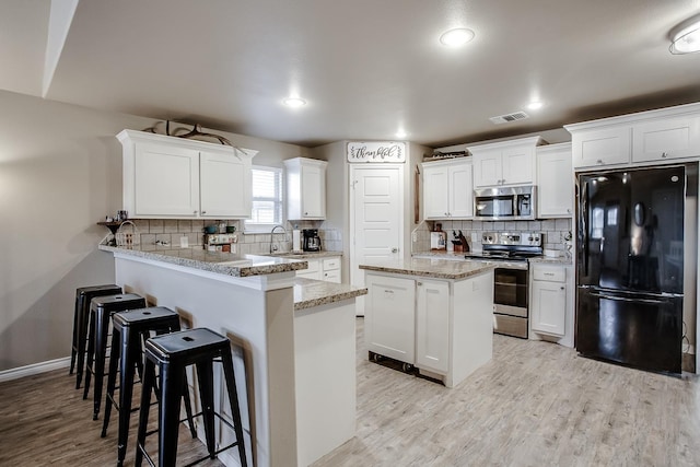 kitchen featuring appliances with stainless steel finishes, light hardwood / wood-style flooring, white cabinets, and kitchen peninsula