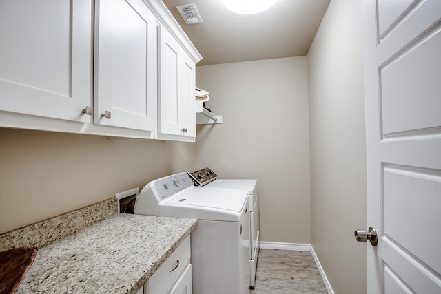 laundry room featuring washer and clothes dryer, light hardwood / wood-style floors, and cabinets