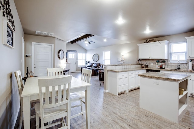 kitchen with white cabinetry, lofted ceiling, a center island, and sink