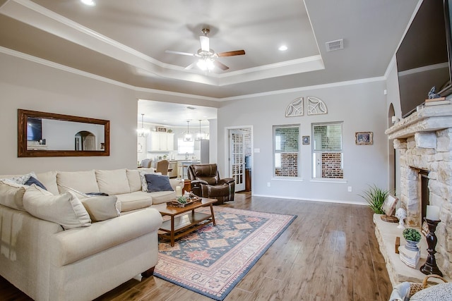 living room with a tray ceiling, a fireplace, ornamental molding, and hardwood / wood-style flooring