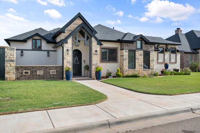 french country style house featuring a front lawn, stone siding, and roof with shingles