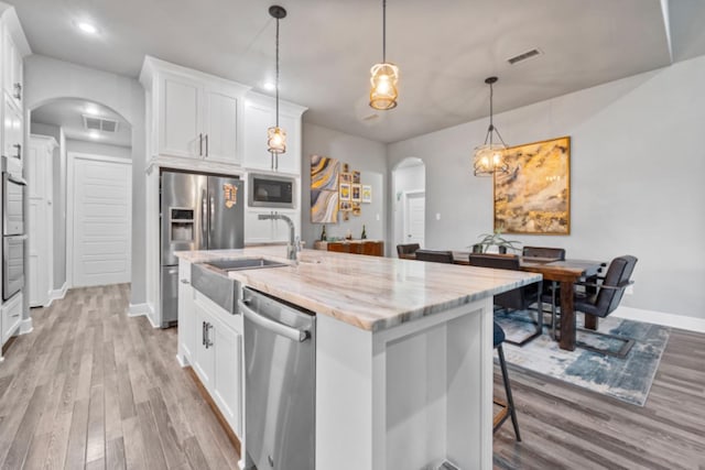 kitchen featuring appliances with stainless steel finishes, pendant lighting, white cabinetry, a kitchen island with sink, and light stone counters