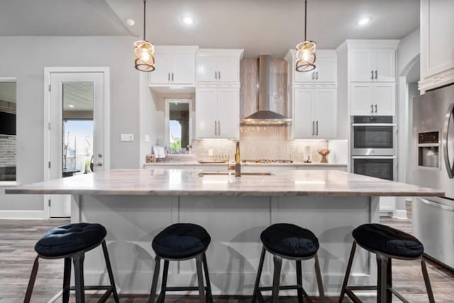 kitchen featuring a kitchen island with sink, wall chimney range hood, and white cabinets