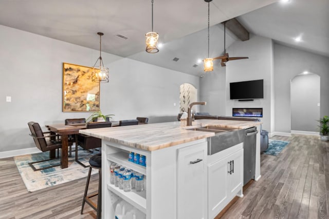 kitchen with pendant lighting, sink, light stone countertops, white cabinets, and a center island with sink