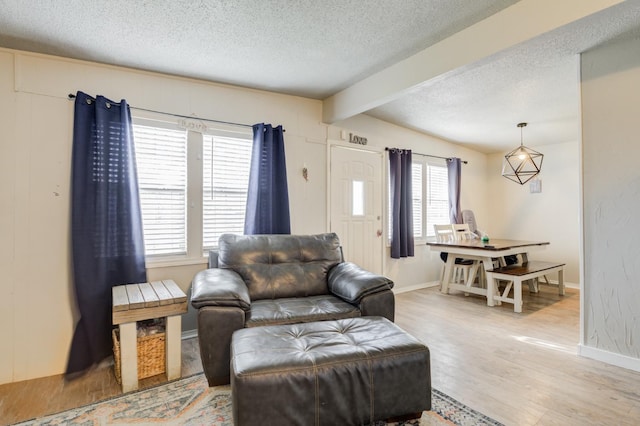 living room with beamed ceiling, a healthy amount of sunlight, light hardwood / wood-style floors, and a textured ceiling