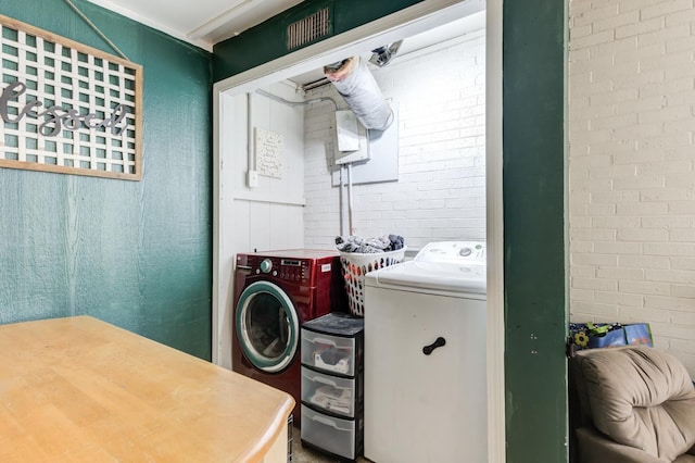 clothes washing area with washer and dryer and brick wall