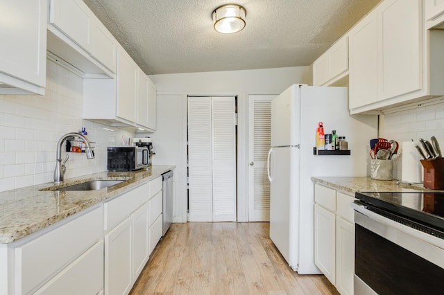 kitchen with appliances with stainless steel finishes, sink, white cabinets, light stone counters, and a textured ceiling