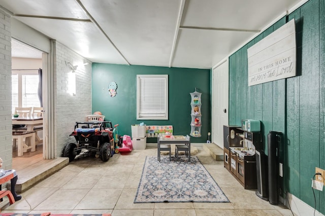 game room featuring light tile patterned flooring, wood walls, and brick wall