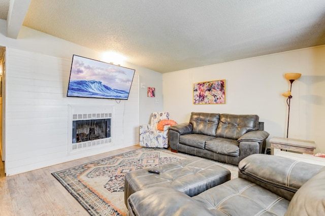 living room featuring beamed ceiling, light hardwood / wood-style floors, and a textured ceiling