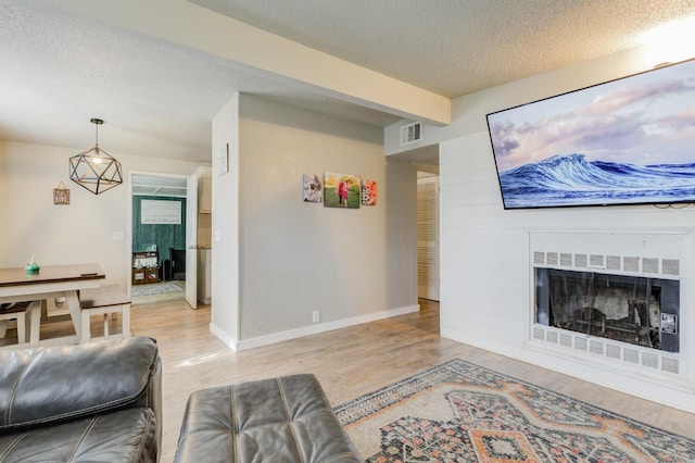 living room featuring beam ceiling, light hardwood / wood-style flooring, and a textured ceiling