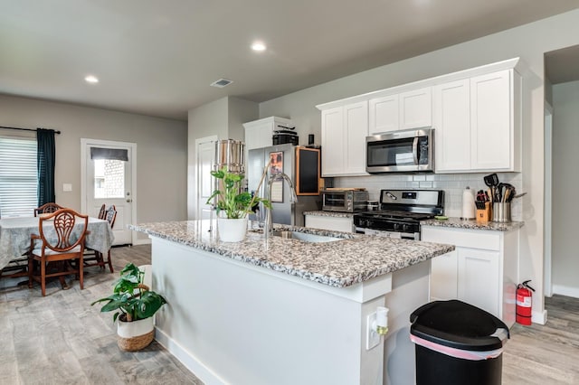 kitchen featuring sink, stainless steel appliances, light stone countertops, a kitchen island with sink, and white cabinets