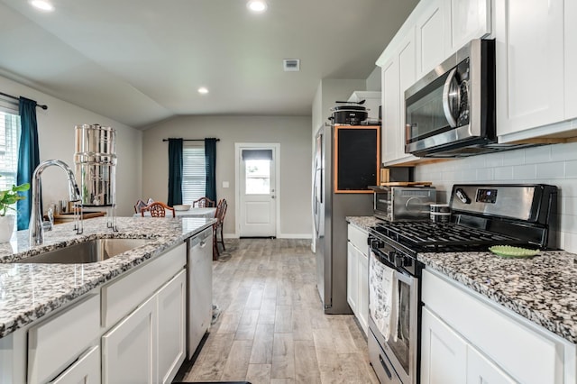 kitchen with sink, white cabinets, stainless steel appliances, light stone countertops, and light wood-type flooring