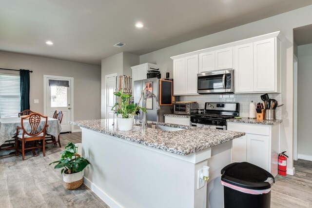 kitchen featuring sink, appliances with stainless steel finishes, white cabinetry, light stone countertops, and an island with sink