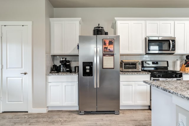 kitchen featuring light stone countertops, stainless steel appliances, and white cabinets