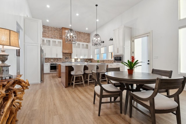 dining area featuring sink, a towering ceiling, light hardwood / wood-style floors, and brick wall