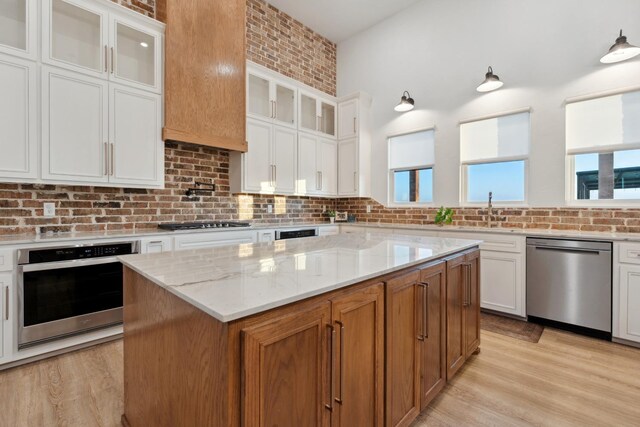 kitchen with stainless steel appliances, light stone countertops, a kitchen island, and white cabinets