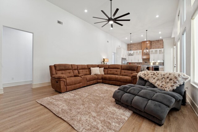 living room featuring a towering ceiling, ceiling fan, and light hardwood / wood-style flooring