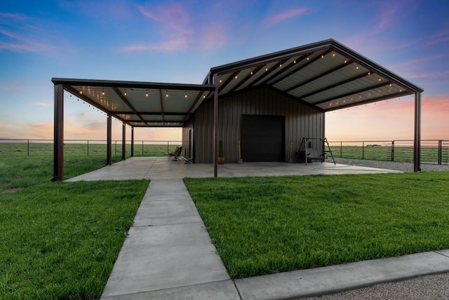 outdoor structure at dusk featuring a garage, a lawn, and a carport