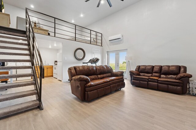 living room with a towering ceiling, french doors, a wall mounted AC, ceiling fan, and light hardwood / wood-style flooring