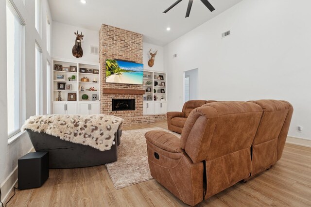 living room featuring ceiling fan, a brick fireplace, light hardwood / wood-style flooring, and a towering ceiling