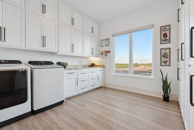 laundry room featuring separate washer and dryer, light hardwood / wood-style flooring, and cabinets