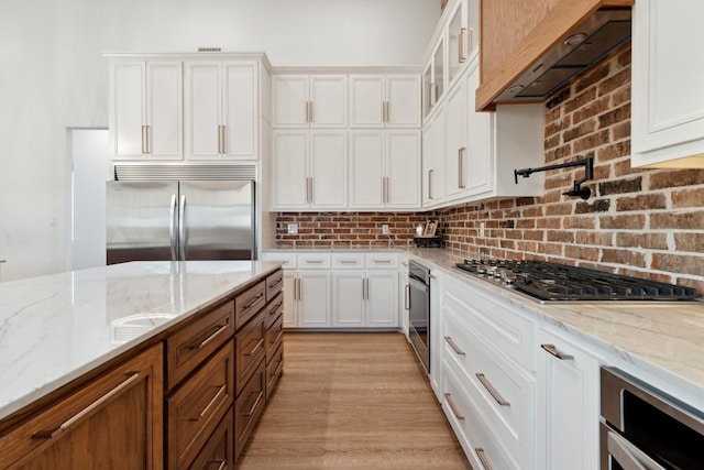 kitchen with white cabinetry, appliances with stainless steel finishes, premium range hood, and light stone counters