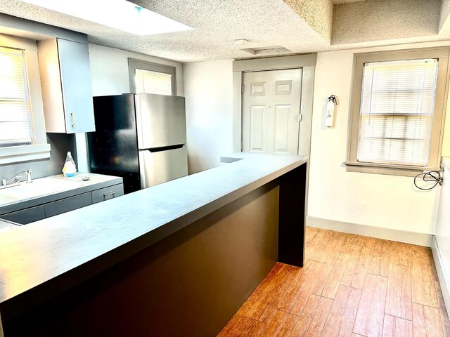 kitchen with light wood-type flooring, gray cabinetry, a textured ceiling, and stainless steel refrigerator