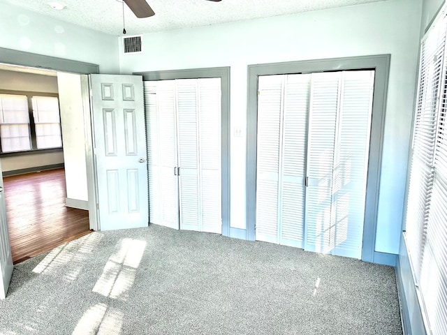 unfurnished bedroom with multiple closets, ceiling fan, and a textured ceiling