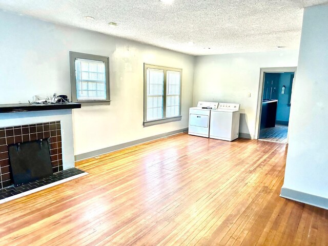 unfurnished living room with a tile fireplace, light wood-type flooring, a textured ceiling, and independent washer and dryer