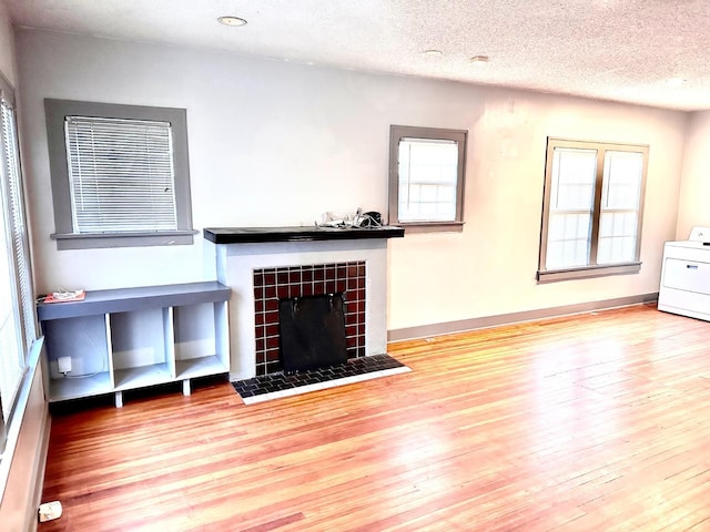 unfurnished living room featuring a healthy amount of sunlight, wood-type flooring, washer / dryer, and a tile fireplace