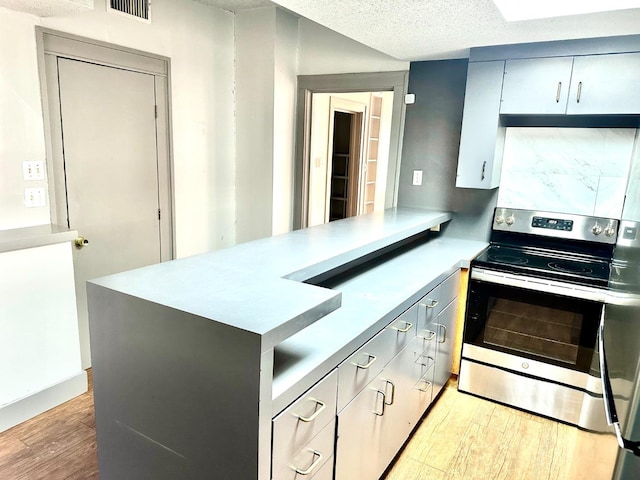 kitchen with gray cabinets, stainless steel electric range oven, kitchen peninsula, a textured ceiling, and light hardwood / wood-style flooring