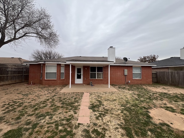 rear view of property featuring a patio, a fenced backyard, brick siding, and a chimney