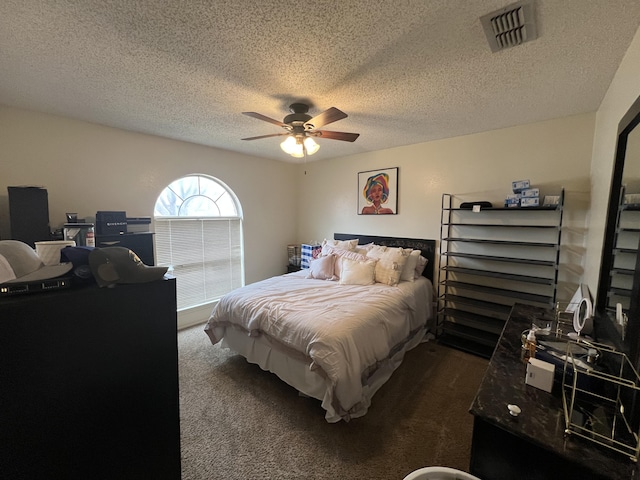 bedroom featuring a ceiling fan, visible vents, dark carpet, and a textured ceiling