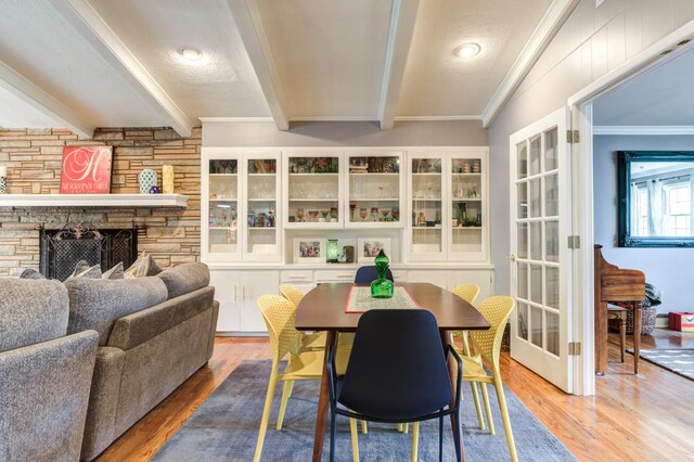 dining room featuring ornamental molding, a stone fireplace, wood-type flooring, and beam ceiling