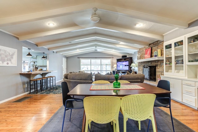 dining space featuring vaulted ceiling with beams, a stone fireplace, and light wood-type flooring