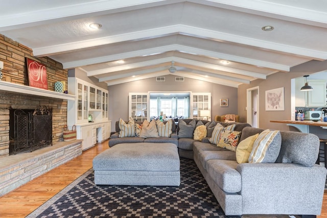 living room featuring a stone fireplace, lofted ceiling with beams, and light hardwood / wood-style flooring