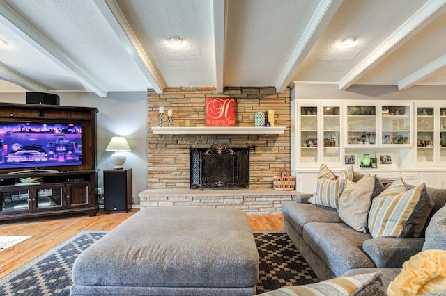 living room featuring beam ceiling, a stone fireplace, light hardwood / wood-style floors, and a textured ceiling