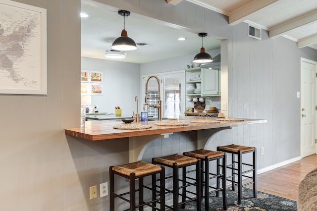 bar featuring hardwood / wood-style floors, decorative light fixtures, beamed ceiling, green cabinets, and crown molding