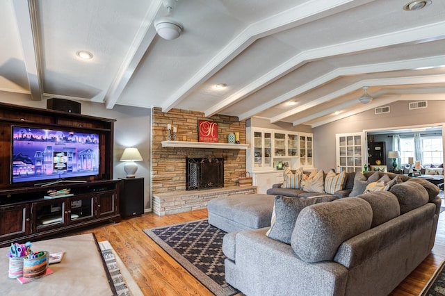 living room featuring vaulted ceiling with beams, a stone fireplace, hardwood / wood-style floors, and ceiling fan