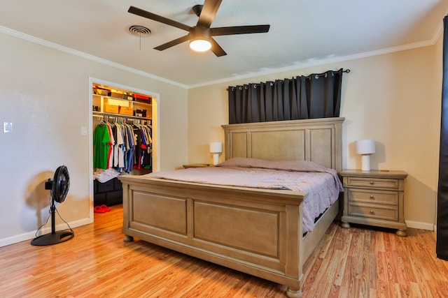 bedroom featuring a spacious closet, light wood-type flooring, ornamental molding, a closet, and ceiling fan